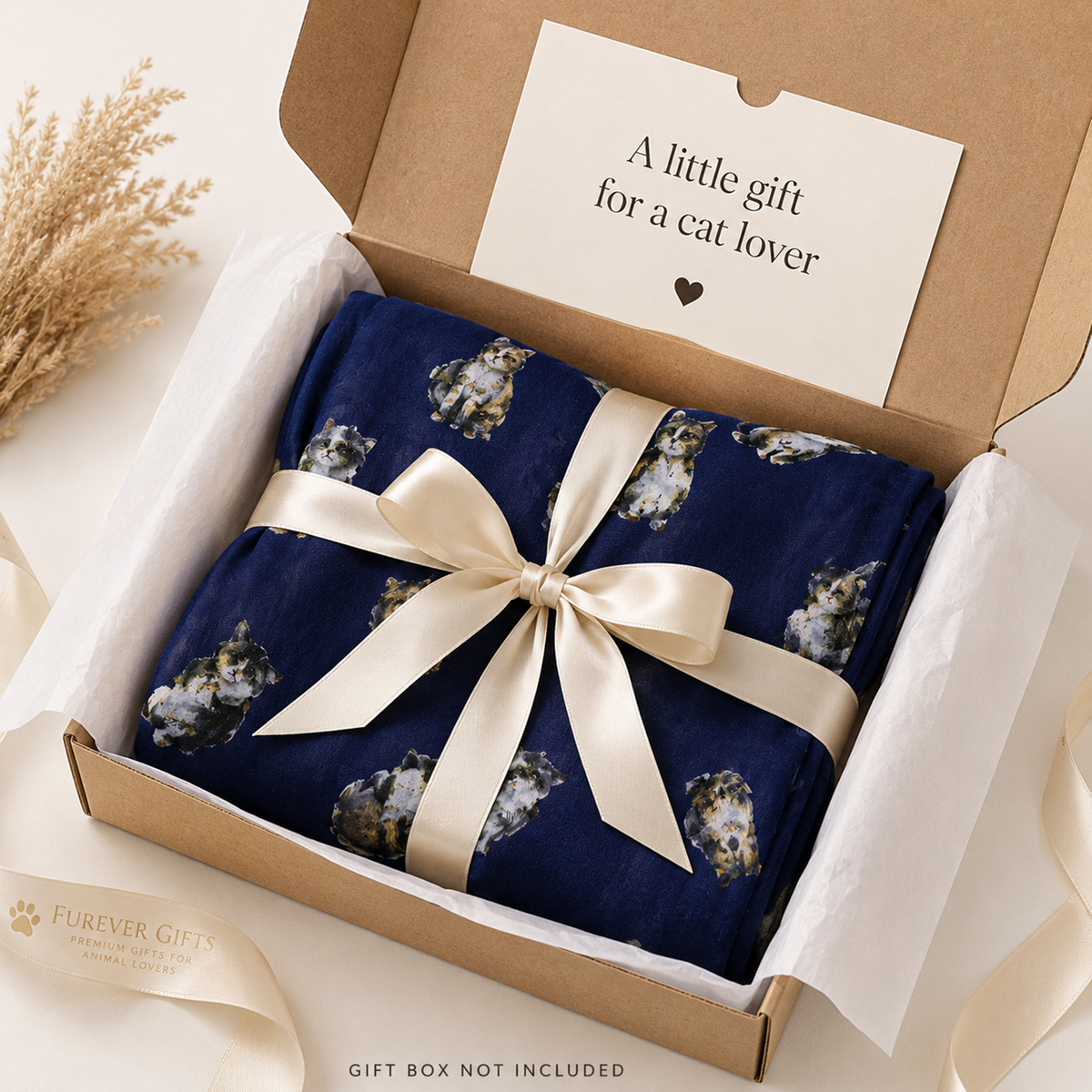 A navy blue blanket with a white and grey cat pattern, wrapped in a cream satin ribbon and presented in a brown cardboard gift box with a printed message card inside. A cream ribbon with 'Forever Gifts' branding is visible in the foreground.