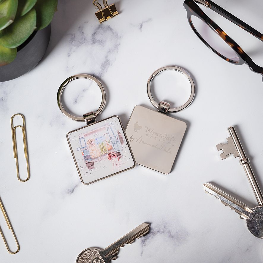 Two keychains on a marble surface with keys and a plant in the background.