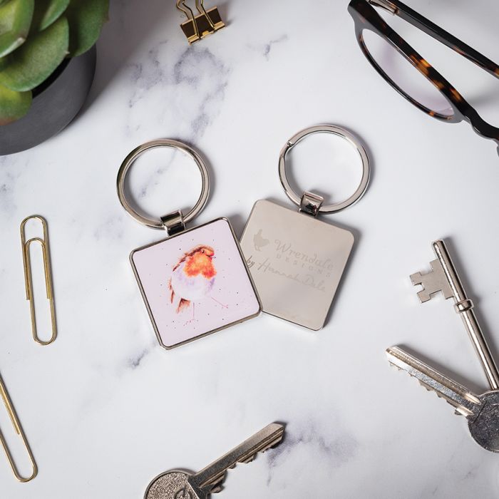 Two keychains on a marble surface with keys and glasses around