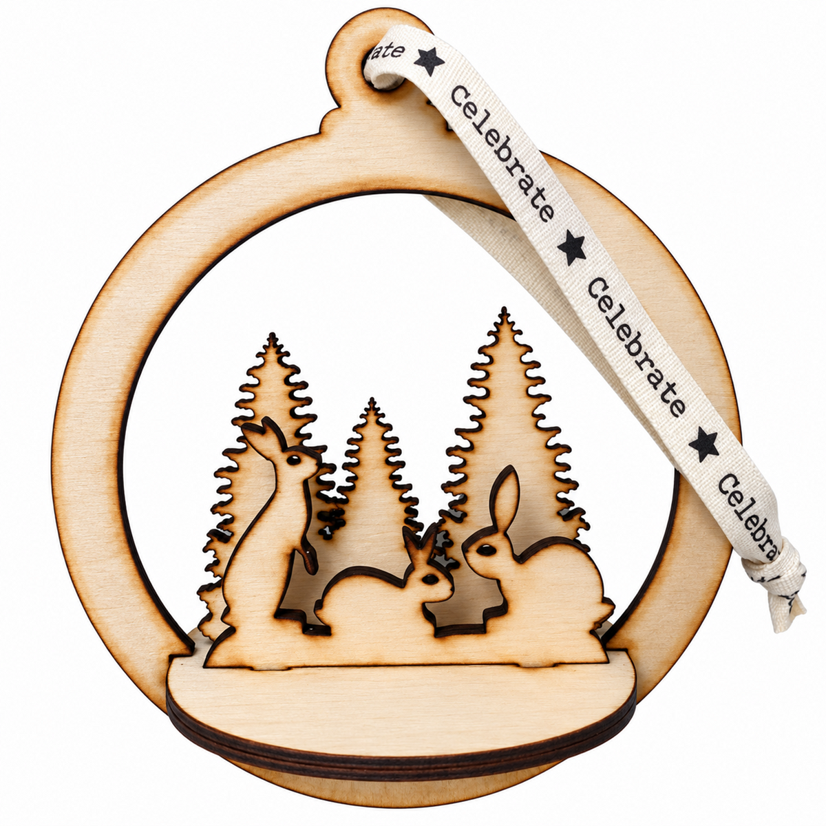 A laser-cut wooden Christmas ornament featuring a deer, rabbit, and pine trees silhouette, hanging from a cream ribbon printed with the word 'Celebrate'.