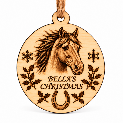 A round wooden Christmas ornament engraved with a horse head, the text 'BELLA'S CHRISTMAS,' snowflakes, holly leaves, and a horseshoe, hanging from a natural wood string on a white background.