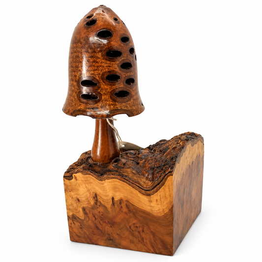 A handcrafted wooden sculpture of a mushroom, featuring a glossy, highly figured burl wood cap with multiple drilled holes and a thick, sculptural base with a live edge, set against a plain white background.