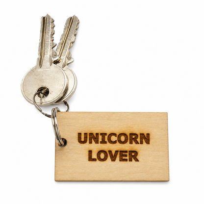 A wooden keychain tag engraved with 'UNICORN LOVER' in dark brown lettering, attached to a metal keyring with two silver keys, shown on a plain white background.