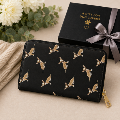 A black zip-around wallet with a repeating print of Chihuahua dogs, styled on a beige surface next to a black gift box with gold lettering and a gray ribbon.