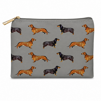 A grey zipped cosmetic bag featuring an all-over print of dachshund dogs in tan and black, with a gold zipper pull, shown on a plain white background.