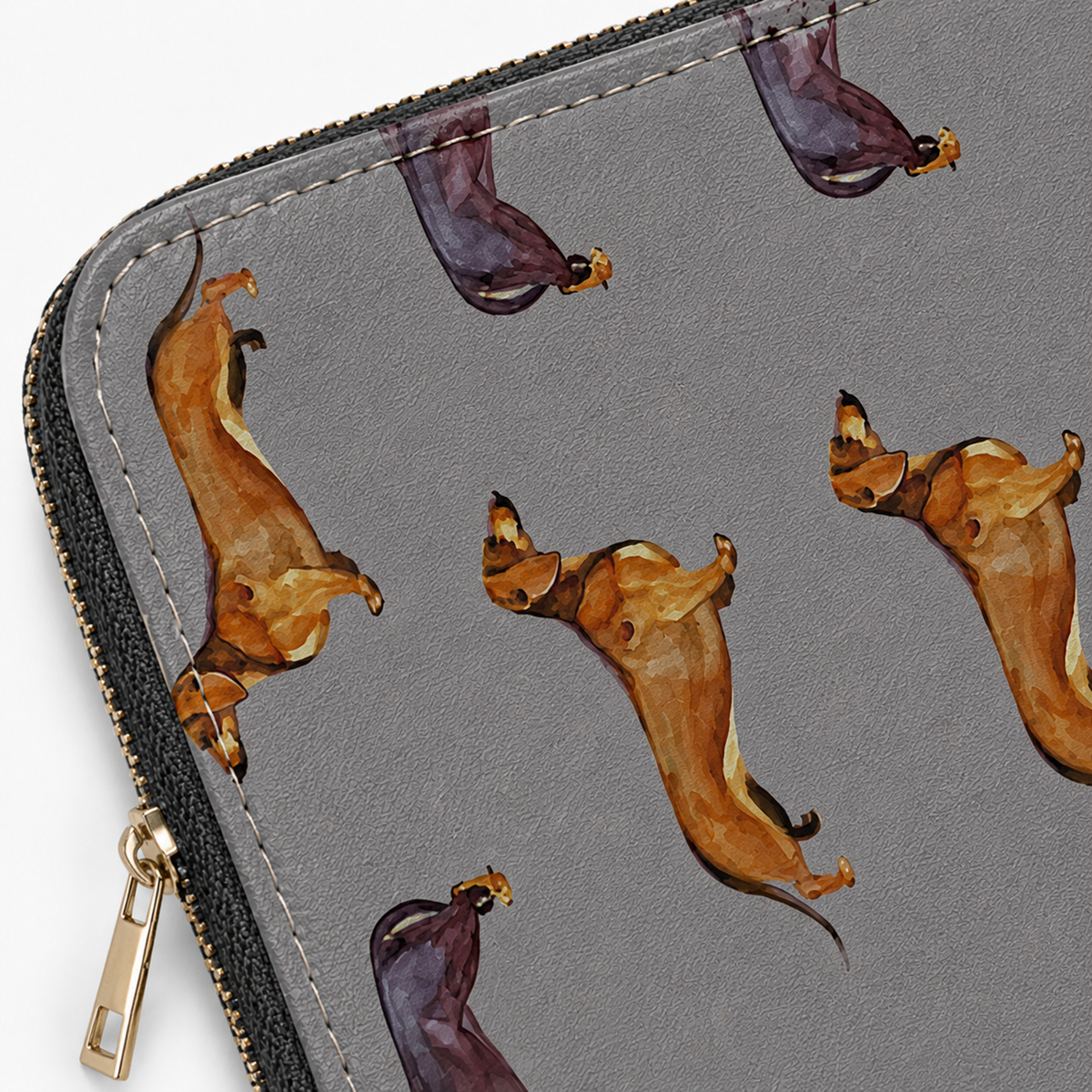 Close-up of a grey zipped pouch or wallet with a repeating watercolour-style print of dachshunds in tan, brown, and dark purple tones, plus black-and-gold zipper trim and stitching.