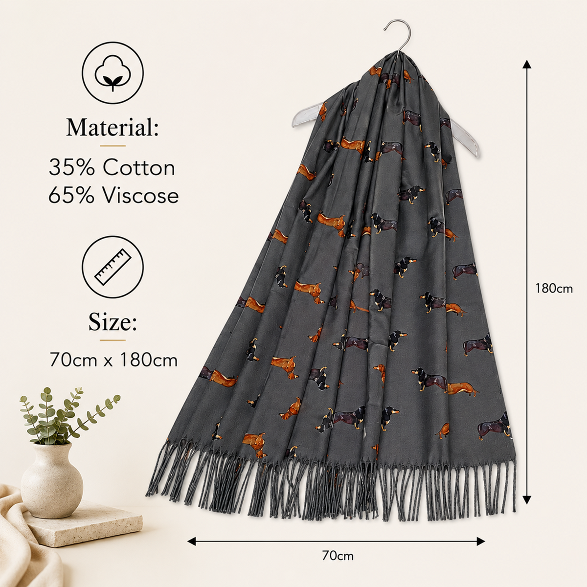 A dark grey patterned scarf with fringe, hanging on a hanger against a light beige background. The scarf features a repeating print of dachshund dogs in tan, black, and brown.