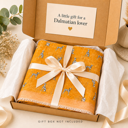 A folded orange scarf with a black and white dalmatian dog print is wrapped in a cream satin ribbon and presented in a brown gift box with tissue paper. The inside lid of the box has a card that reads 'A little gift for a Dalmatian lover'.