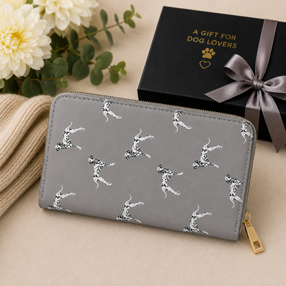 A grey zip-around wallet with a black-and-white dalmatian dog print pattern, styled on a beige surface next to a black gift box with gold lettering and a grey ribbon.