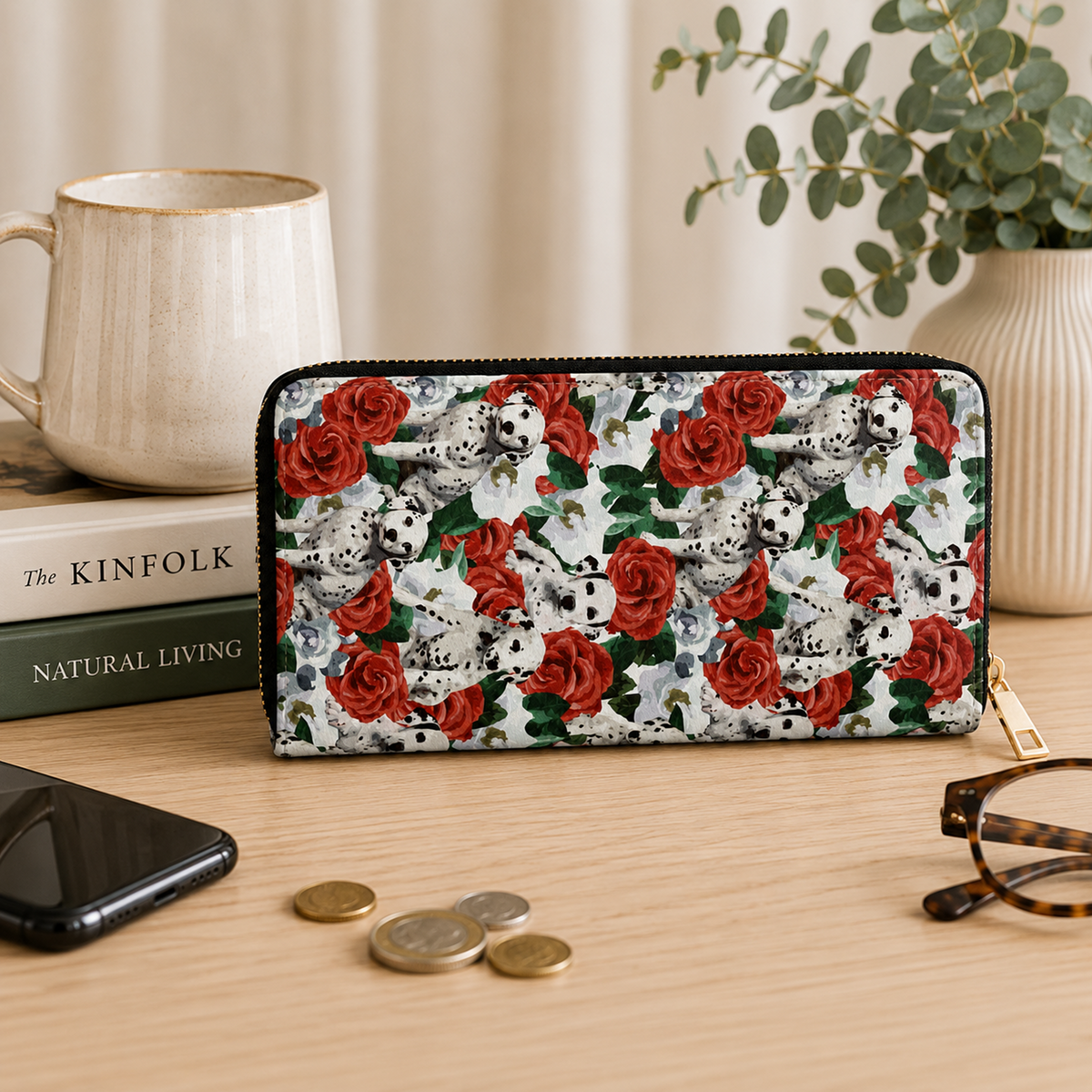 A zip-around wallet with a Dalmatian and red rose pattern, displayed on a wooden desk with a mug, books, phone, coins, and eyeglasses in a styled home setting.