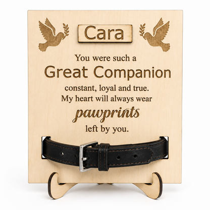 Personalised wooden pet memorial plaque on a small wooden stand, engraved with the name Cara and a pawprint-themed remembrance message, with a black leather collar displayed across the front.