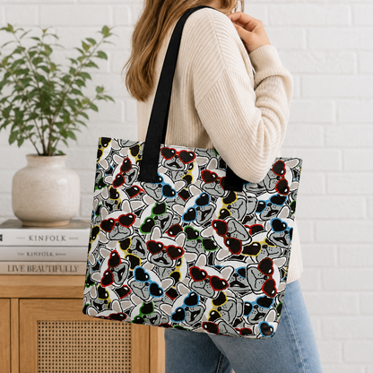 A woman wearing a cream ribbed sweater and blue jeans carries a large tote bag with a black handle. The tote bag features an all-over print of stylized cartoon French Bulldogs in multiple colours on a white background.