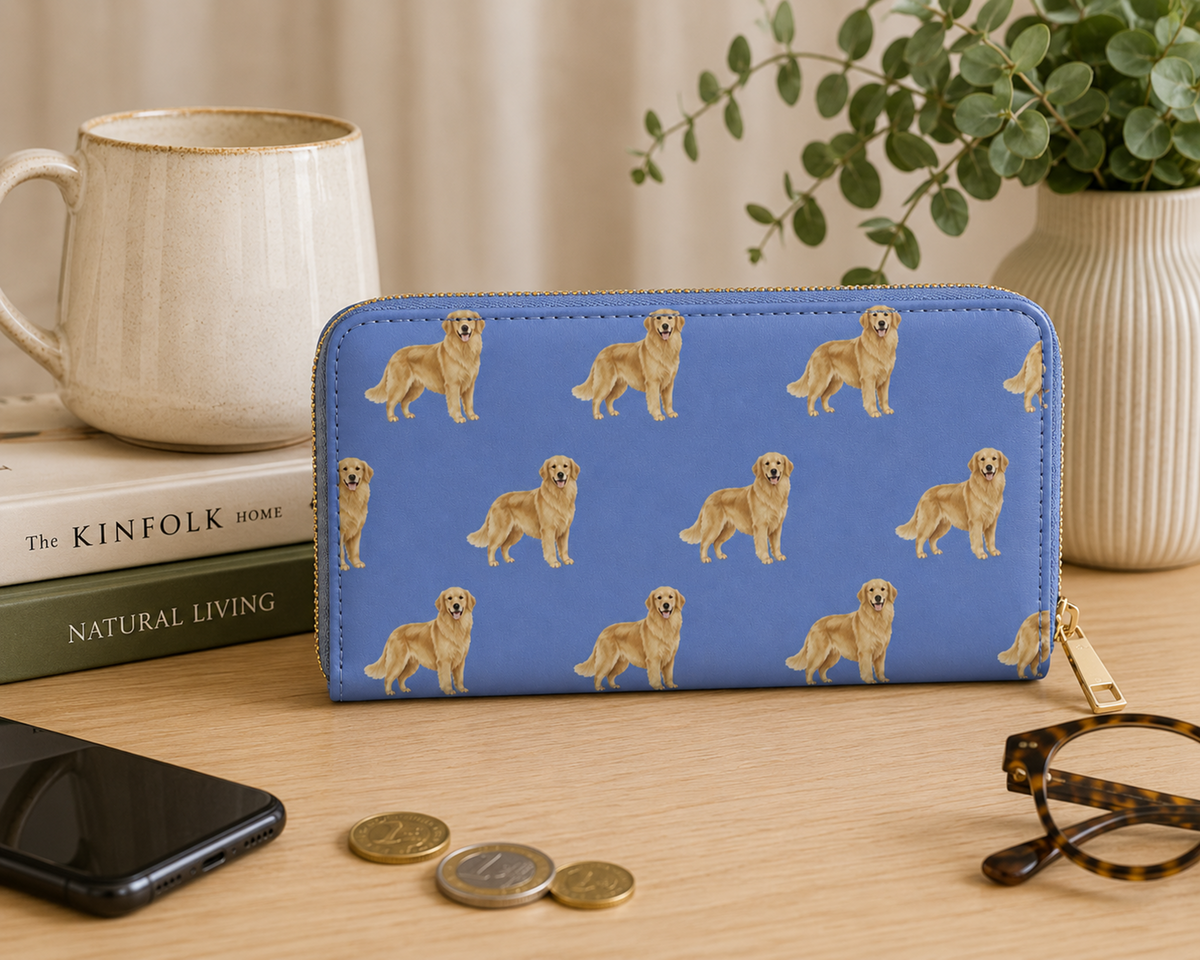 A blue zip-around wallet with a repeating pattern of golden retriever dogs, styled on a wooden tabletop with a mug, books, a phone, coins, eyeglasses, and a potted plant in the background.