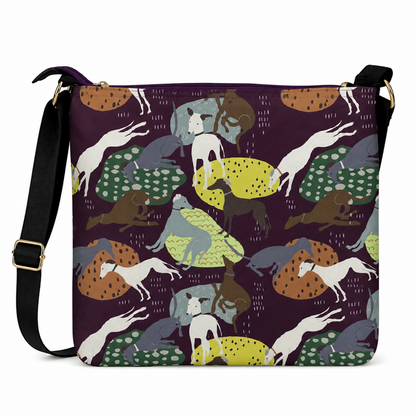 A square crossbody bag with a dark purple background and an all-over whimsical pattern of Greyhound dogs in white, brown, grey, green, and yellow. The bag has a black shoulder strap with gold-tone hardware.