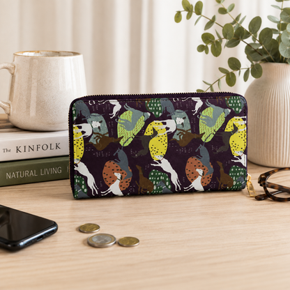 A zip-around wallet with a colourful Greyhound & Whippet dog pattern, styled on a wooden tabletop next to a smartphone, coins, eyeglasses, a mug, and books.