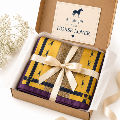A luxury silk equestrian headscarf with a gold base, textured mustard panels, and burgundy borders, featuring small black monogram motifs and gold-tone hardware. Displayed in a gift box.