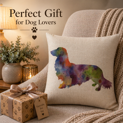 A square beige cushion cover pillow with a colourful watercolour-style dog silhouette, styled on a cream armchair beside a wrapped gift box and a cosy knit blanket. Text in the upper left reads 'Perfect Gift for Dog Lovers' with paw and heart icons.