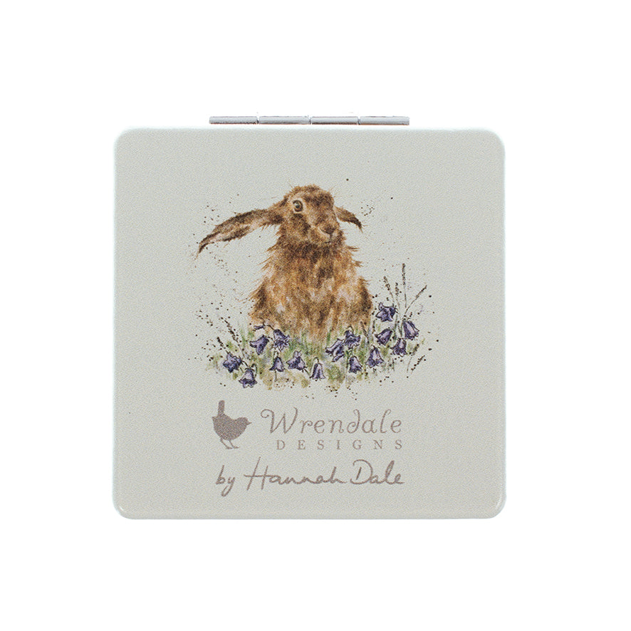 A square compact case with rounded corners featuring a watercolor illustration of a brown hare among purple flowers. The brand name 'Wrendale Designs by Hannah Dale' is printed below the illustration on a light gray background.
