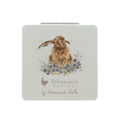 A square compact case with rounded corners featuring a watercolor illustration of a brown hare among purple flowers. The brand name 'Wrendale Designs by Hannah Dale' is printed below the illustration on a light gray background.