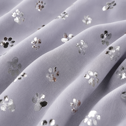 A close-up of sheer lavender-gray fabric with scattered silver sequin floral motifs and paw print embellishments.