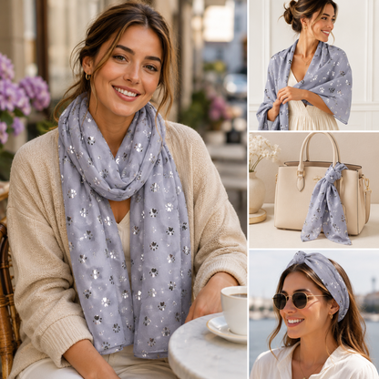 A women's lightweight scarf shown in three lifestyle and styled views: worn draped around the neck, tied over the shoulders, and styled with a matching headband. The scarf is a soft dusty lavender-grey with scattered small metallic silver paw print motifs.
