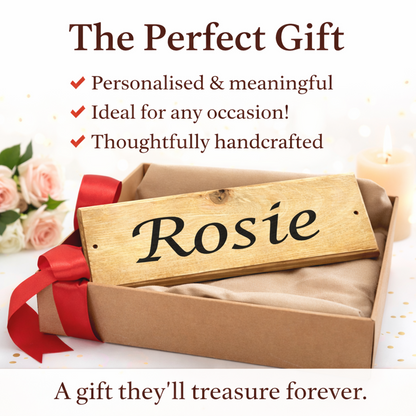 A personalised wooden horse stable door name plaque engraved with the name 'Rosie' rests inside a brown gift box lined with beige fabric and tied with a red ribbon. The scene is styled with pink roses, a lit candle, and promotional text reading 'The Perfect Gift' and 'A gift they'll treasure forever.