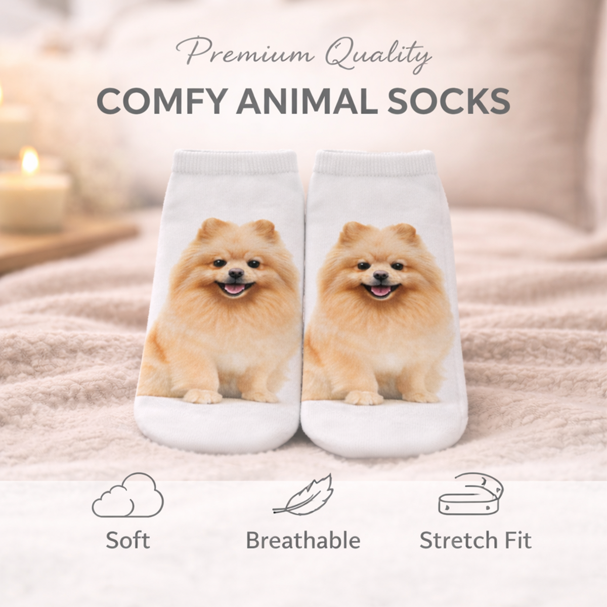 A pair of white trainer socks printed with two smiling Pomeranian dogs, displayed on a soft beige blanket with candles in the background. Text at the top reads 'Premium Quality COMFY ANIMAL SOCKS' and icons at the bottom highlight soft, breathable, and stretch-fit qualities.