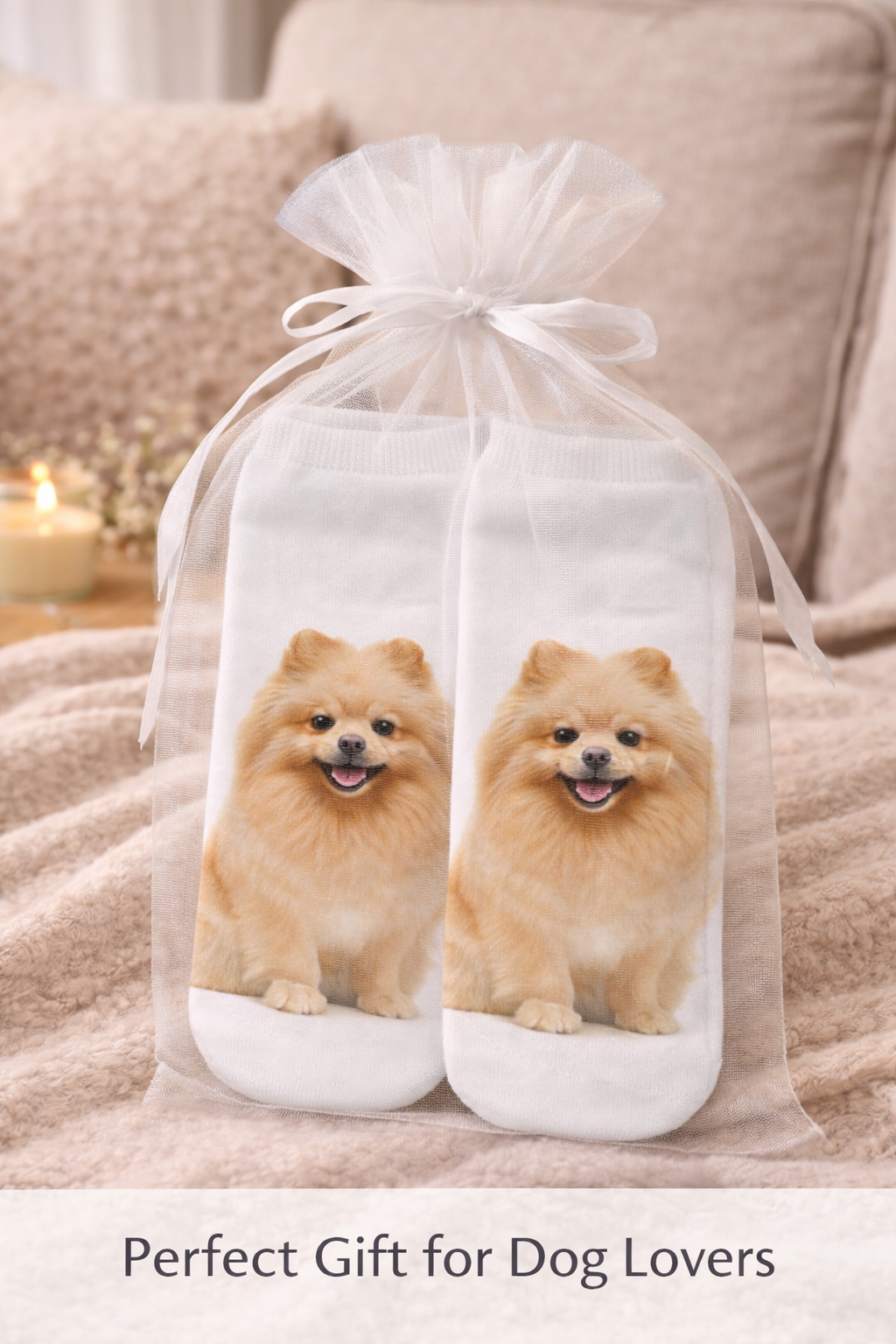A pair of white socks with printed images of a fluffy golden Pomeranian dog, packaged in a clear sheer gift bag tied with a white ribbon, set against a coz living room background with a lit candle.