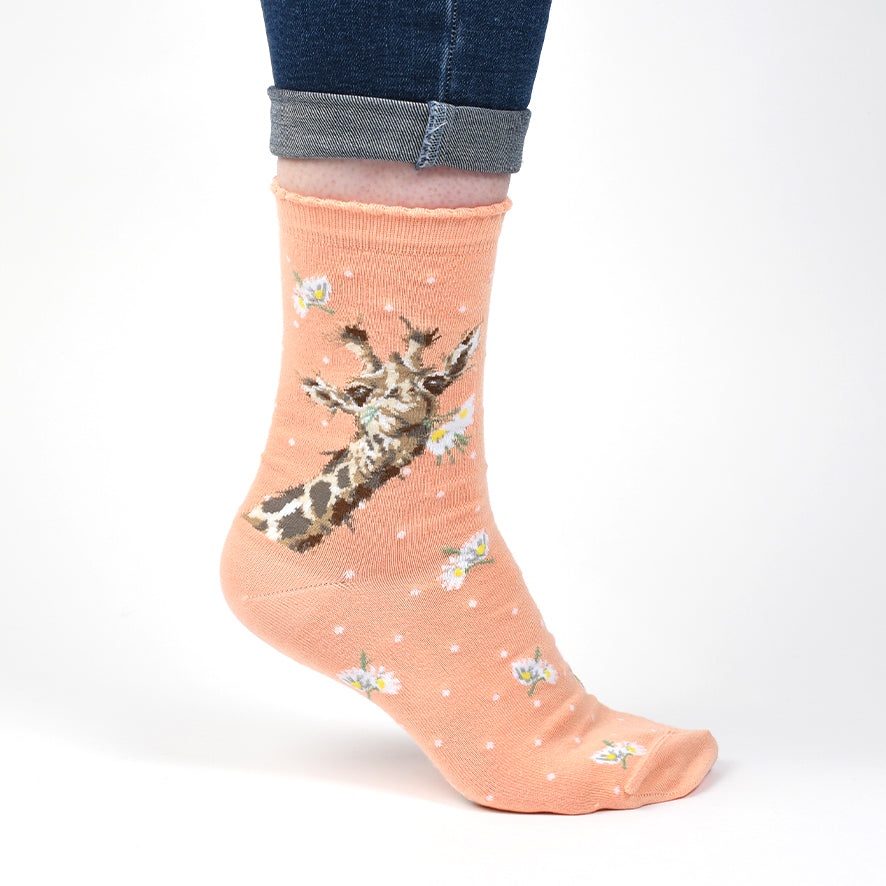 Peach-colored sock with a giraffe design worn by a person on a white background