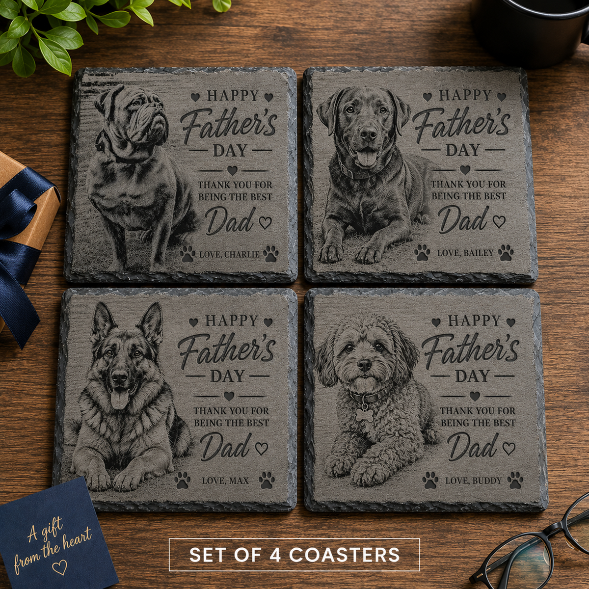 Four personalised slate coasters arranged in a 2x2 grid on a wooden table, each engraved with a different dog portrait and the text 'Happy Father's Day' plus a thank-you message. A small gift box with a blue ribbon appears at lower left, and eyeglasses are at lower right.