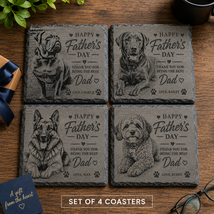 Four personalised slate coasters arranged in a 2x2 grid on a wooden table, each engraved with a different dog portrait and the text 'Happy Father's Day' plus a thank-you message. A small gift box with a blue ribbon appears at lower left, and eyeglasses are at lower right.