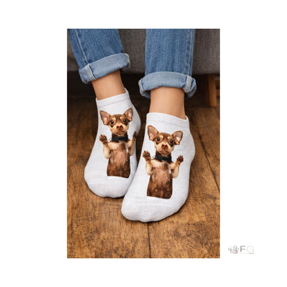 A pair of white ankle socks worn on feet, featuring a printed image of a small brown Chihuahua dog on each sock, shown with cuffed blue jeans on a wooden floor.