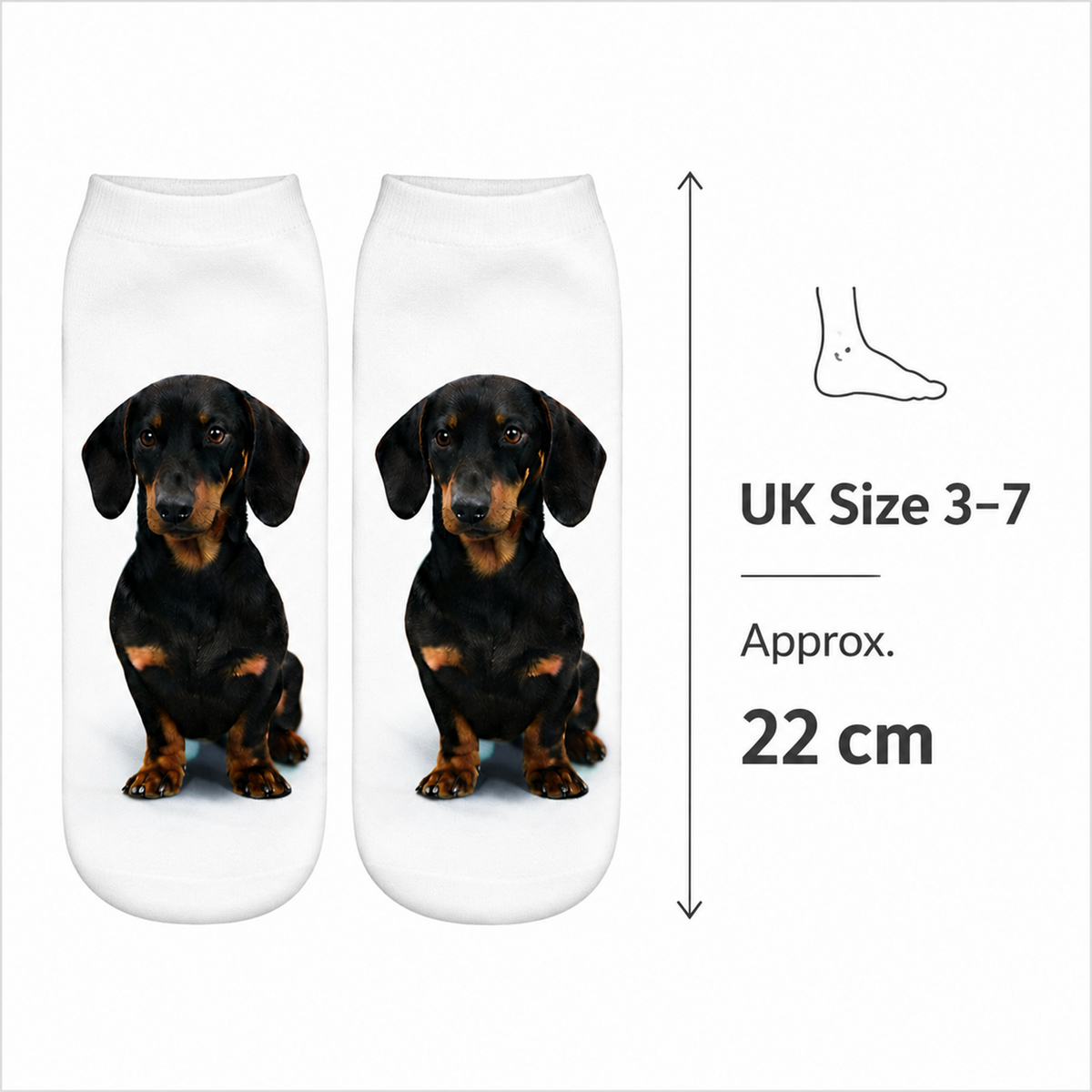 A pair of white ankle socks with a printed black and tan dachshund dog face, shown on a light gray background with size information reading UK Size 3-7 and 22 cm.