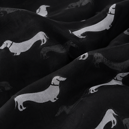 Black scarf with a repeating pattern of white dachshund dog silhouettes, shown in a close-up draped view.