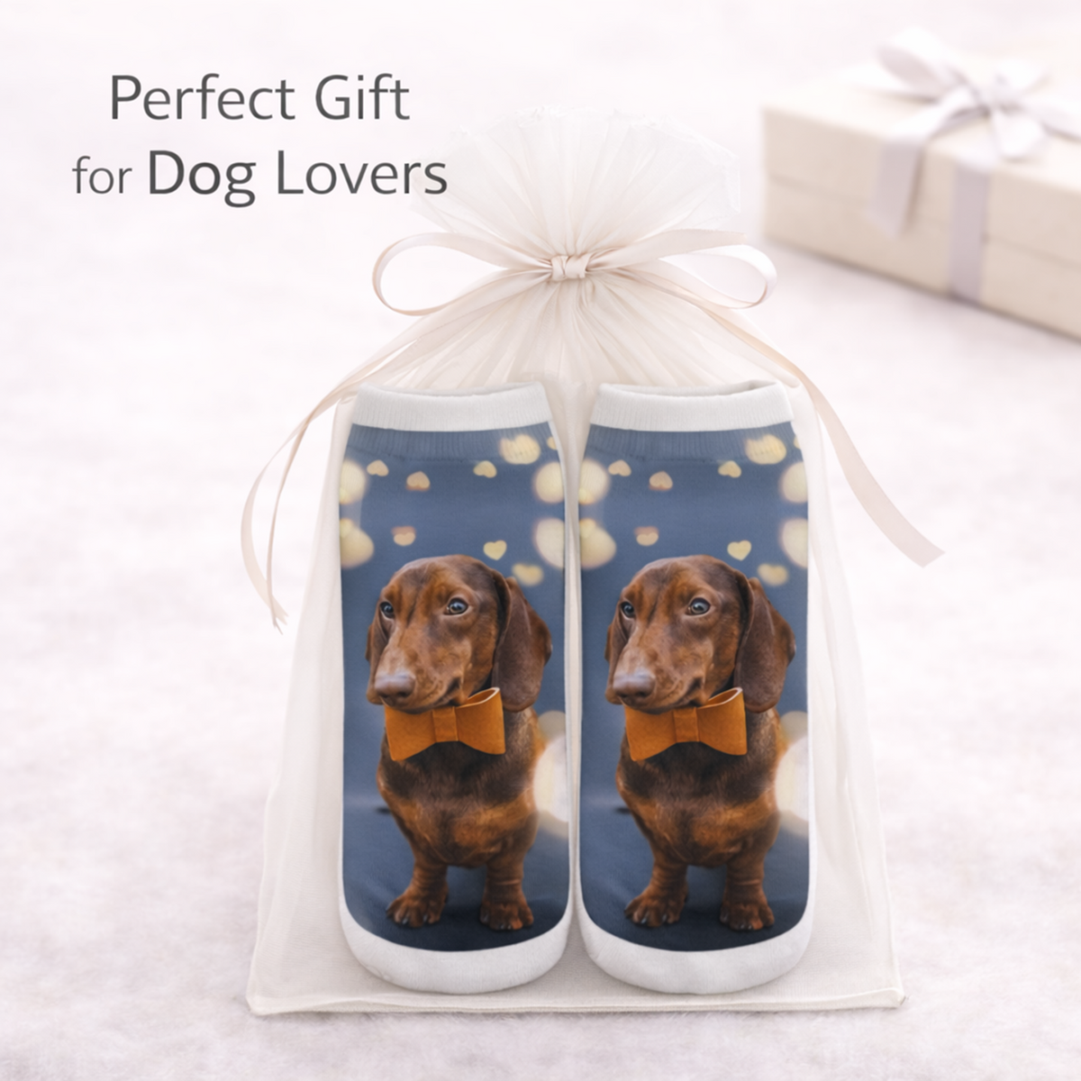 A pair of custom dog socks packaged in a white organza gift bag tied with a ribbon, with a dachshund printed on the socks against a blue background with gold hearts. Text overlay reads 'Perfect Gift for Dog Lovers'.