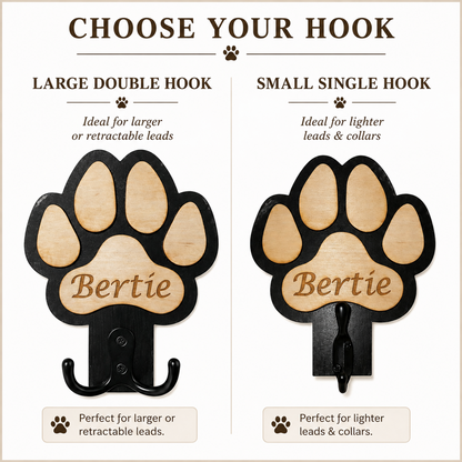 A product comparison graphic showing two versions of a paw-shaped pet name dog lead holder: a large double hook labelled 'LARGE DOUBLE HOOK' and a small single hook labelled 'SMALL SINGLE HOOK.' Both hooks have a black metal frame and a light natural wood paw pad with the name 'Bertie' engraved.