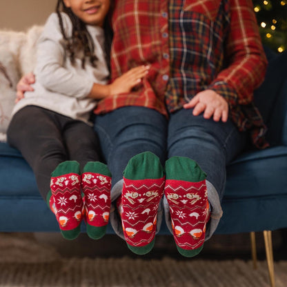 A person and a child sitting on a blue couch with their legs raised, wearing matching Wrendale Designs Season's Tweetings socks with green toes and white snowflake and fish patterns.