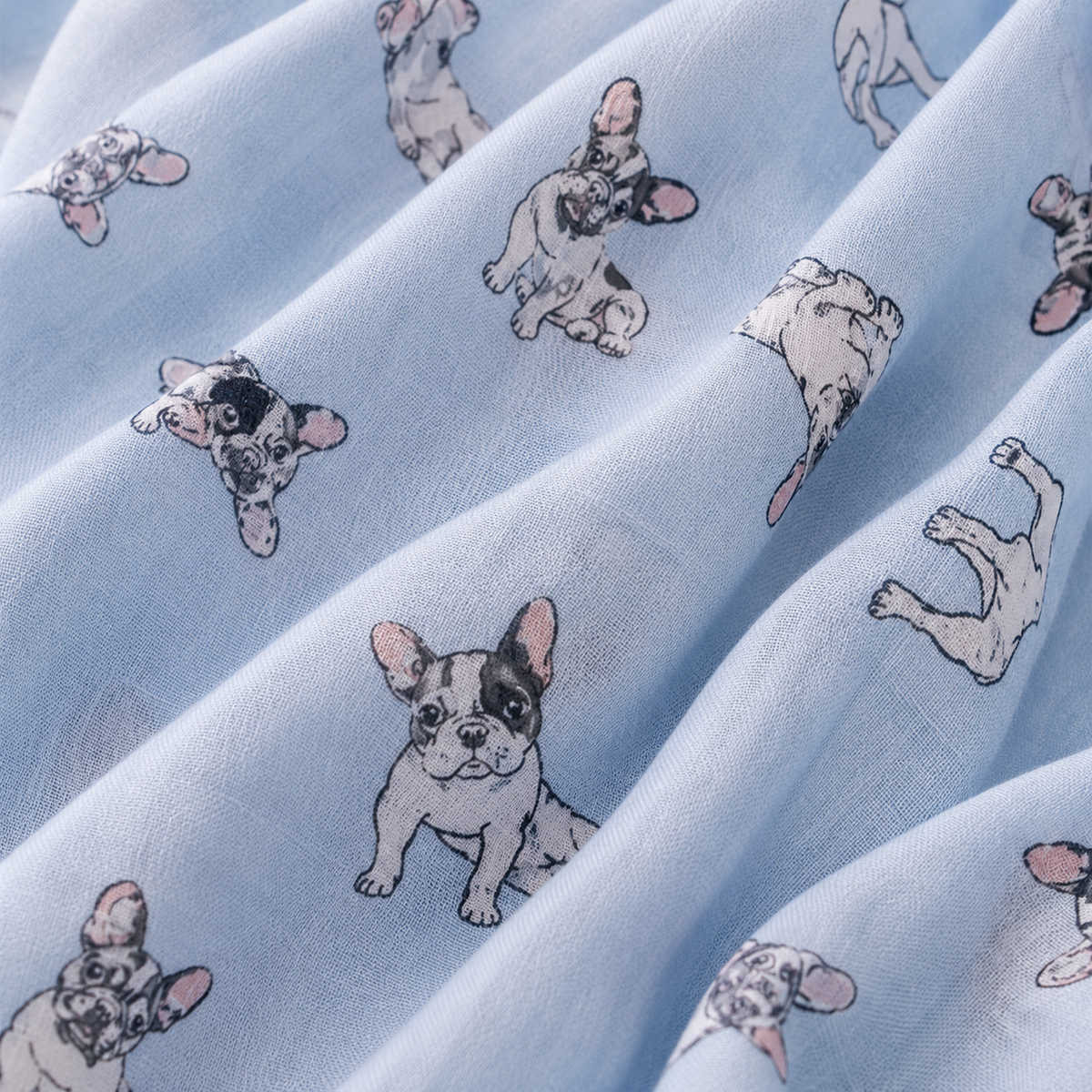 Light blue scarf with a repeating print of French bulldog illustrations in black, grey, and pink, shown in soft folds.
