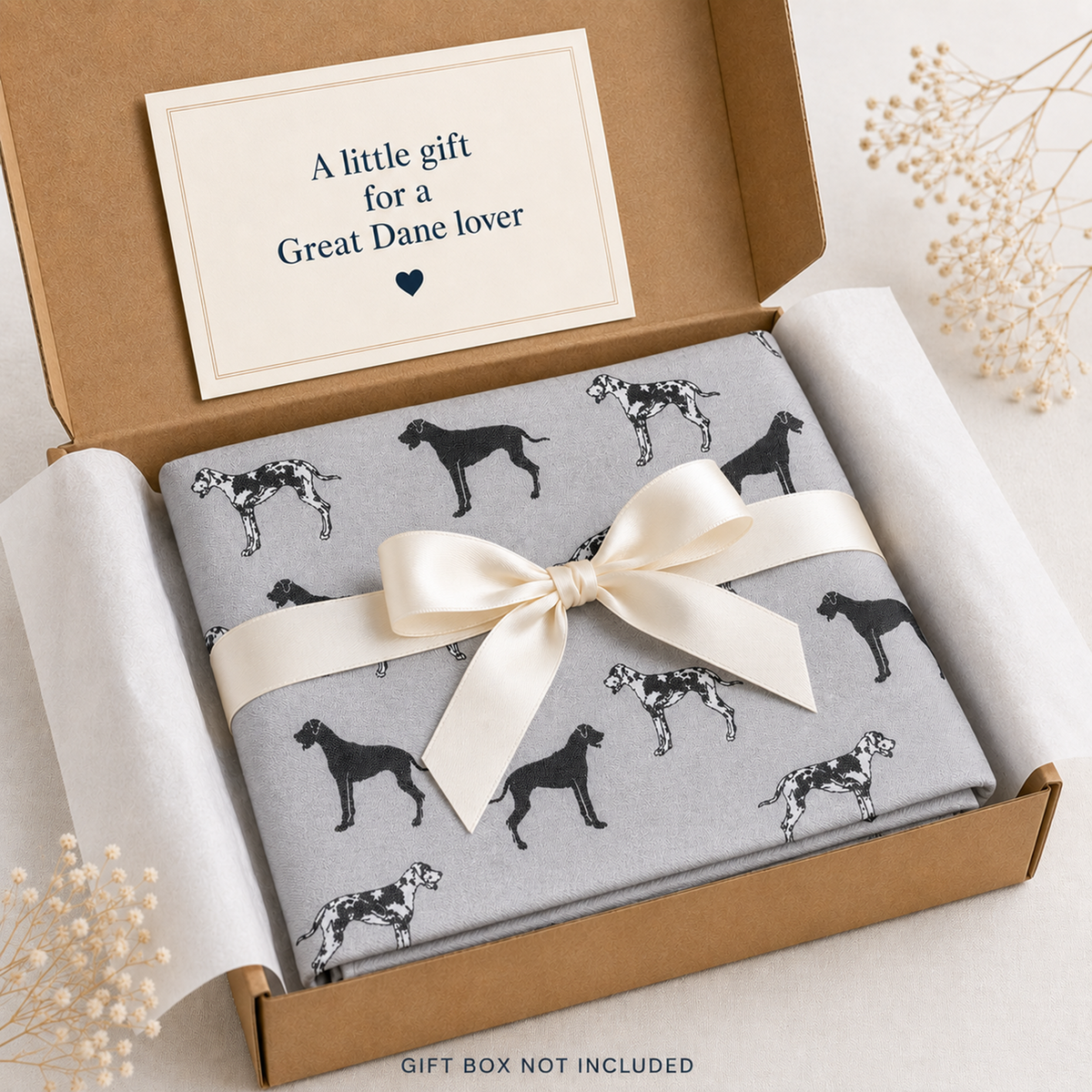 A folded grey scarf gift item with a black Great Dane dog print sits in an open brown box, tied with a cream satin ribbon. A cream card inside the box reads, 'A little gift for a Great Dane lover.