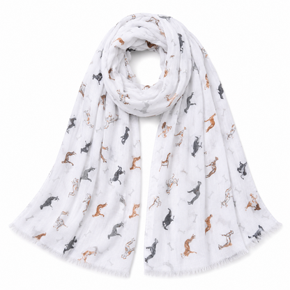 A lightweight white scarf with a scattered print of greyhound whippet dog silhouettes in black, grey, and tan, finished with fringed edges and styled in a loose loop on a white background.
