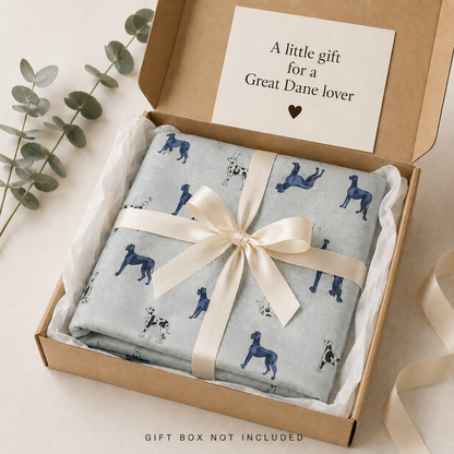 A folded gift box wrapped in a light blue scarf printed with Harlequin Great Dane dogs, tied with a cream satin ribbon and presented in a kraft gift box. A card inside the lid reads 'A little gift for a Great Dane lover'.