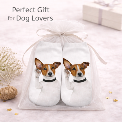 A pair of white socks with printed images of a Jack Russell Terrier dog wearing a black collar, presented in a clear tulle gift bag with a white ribbon. The image includes the text 'Perfect Gift for Dog Lovers' and is styled with decorative elements like dried flowers, twine, and small gold stars on a light pink background.