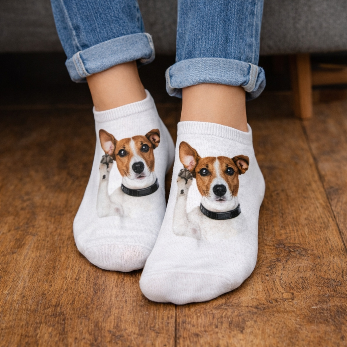 White low-cut socks with a printed image of a Jack Russell Terrier dog, worn by a person in cuffed blue jeans standing on a wooden floor.