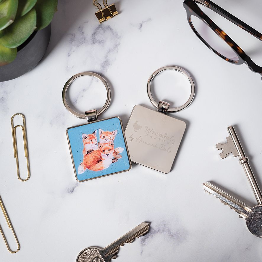 Keychain with fox design and engraved text on a marble surface with keys and glasses.