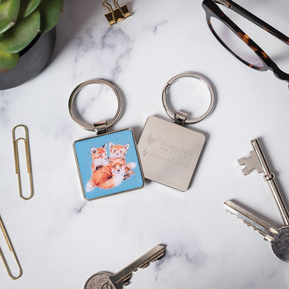 Keychain with fox design and engraved text on a marble surface with keys and glasses.