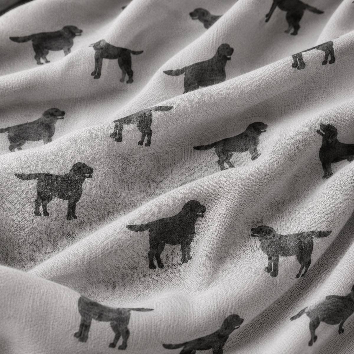 A close-up of draped grey scarf printed with repeating black Labrador dog silhouettes, showing the soft texture and pattern detail.
