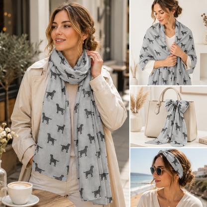 A light grey scarf with a black Labrador dog silhouette pattern, shown worn by a woman in multiple lifestyle settings including outdoors, over the shoulder, and as a headband, alongside a beige handbag.