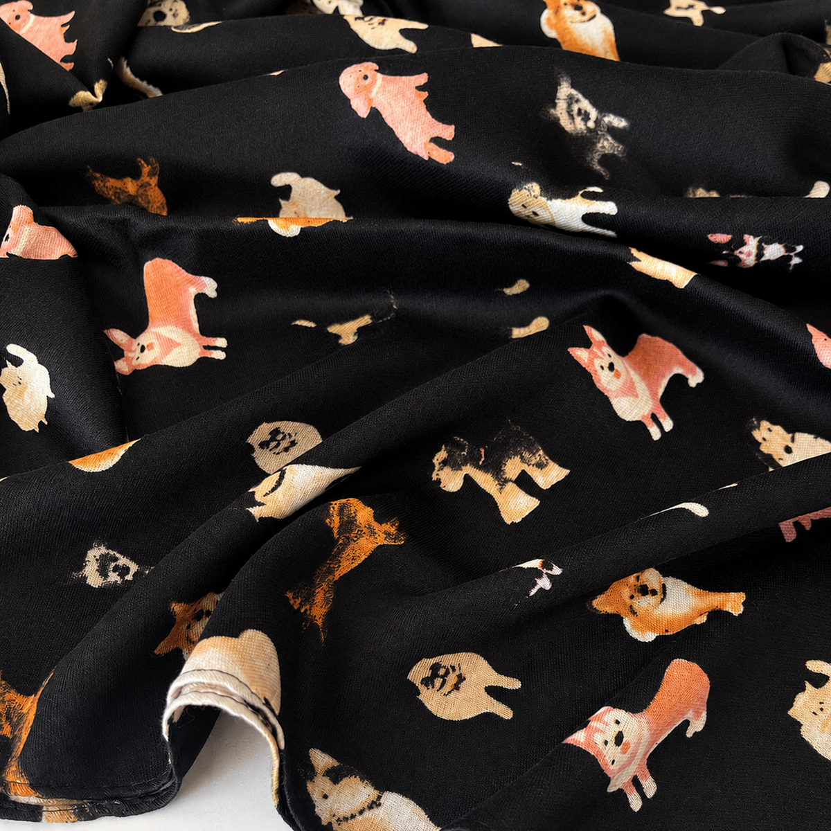 A folded black scarf featuring a playful print of various dog breeds in black, white, beige, and orange, finished with fringed edges.