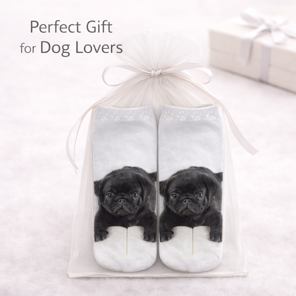 A pair of white ankle socks with a printed black pug puppy design, presented in a clear gift bag with a white ribbon. The text 'Perfect Gift for Dog Lovers' is displayed in the upper left corner.