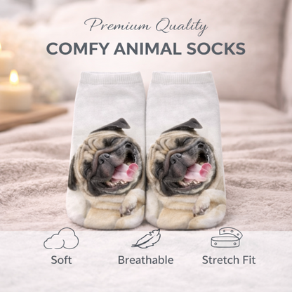 A pair of white novelty socks printed with a pug dog face, shown on a bed with soft blankets and candles in the background. Text at the top reads 'Premium Quality COMFY ANIMAL SOCKS' and feature icons below mention Soft, Breathable, and Stretch Fit.